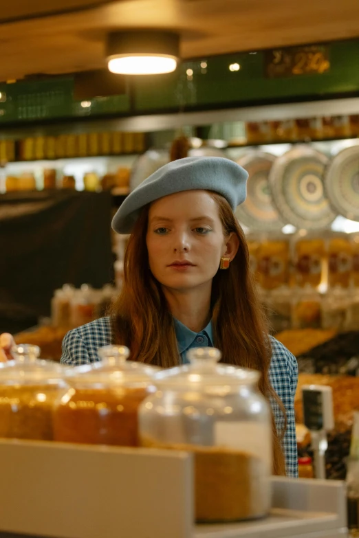 a woman standing behind a counter in a store, a picture, by Anna Boch, trending on pexels, renaissance, wearing a beret, mackenzie foy, pale blue, icon