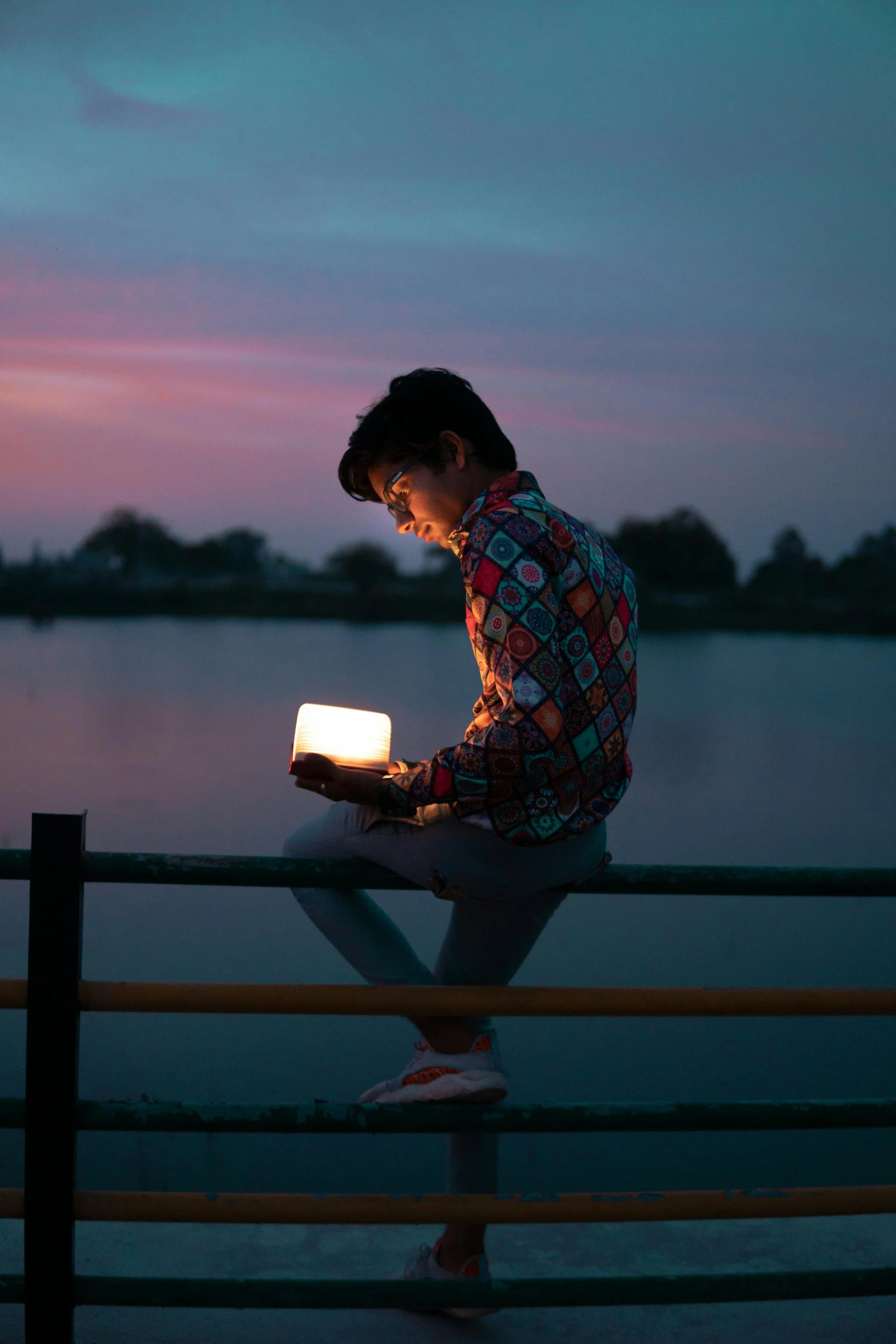 a man sitting on a fence using a laptop, an album cover, by Fei Danxu, unsplash, happening, holding glowing laptop computer, holding a candle, bisexual lighting, sitting in front of a lake