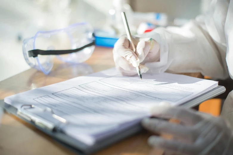 a person in a lab coat writing on a piece of paper, papers on table, background image, multiple stories, surgical supplies