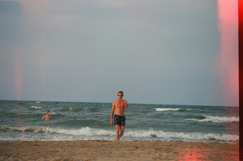 a man standing on top of a sandy beach next to the ocean, in the evening, black sea, zachary corzine, swimming