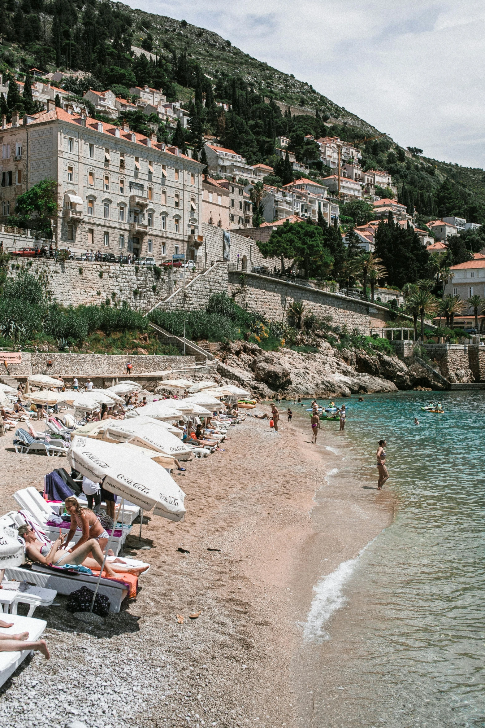 a group of people sitting on top of a sandy beach, dubrovnik, lush surroundings, square, beach aesthetic