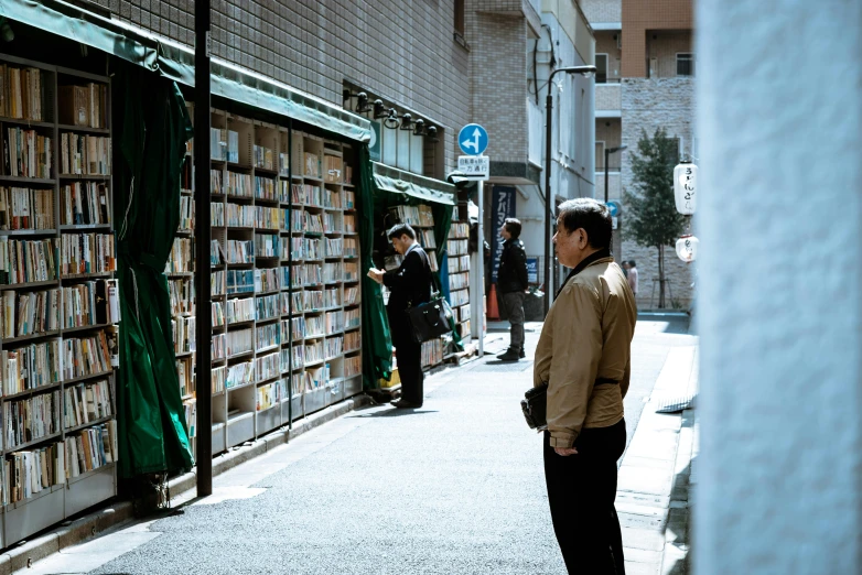 a man standing in front of a book store, a photo, unsplash, ukiyo-e, green alley, sunny day time, people watching around, empty streetscapes