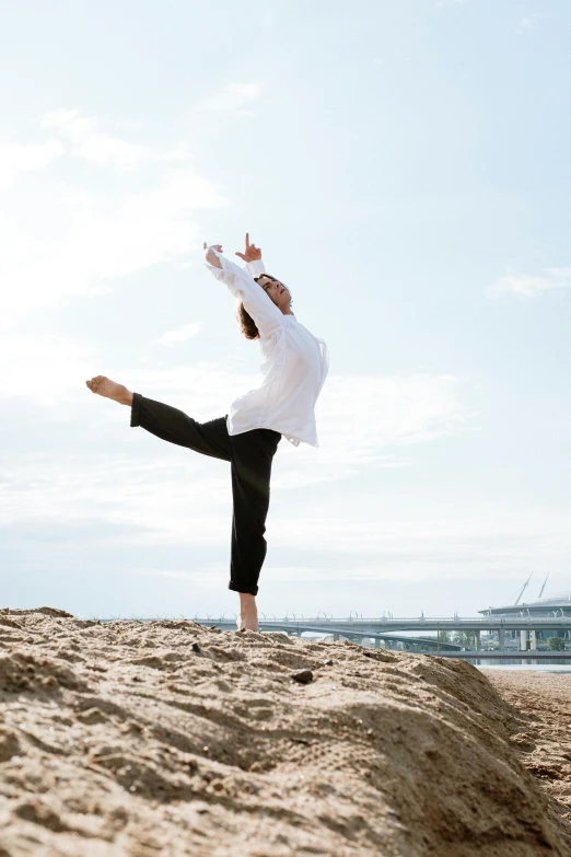 a man standing on top of a sandy beach, arabesque, doing a sassy pose, standing on rocky ground, white, female dancer