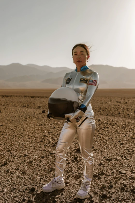 a woman in a space suit holding a helmet, by Alison Geissler, trending on unsplash, conceptual art, mongolia, mojave desert, wearing tight suit, actress