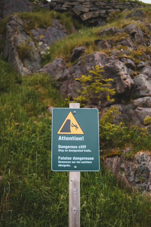 a green sign sitting on top of a lush green hillside, a picture, by Haukur Halldórsson, unsplash, dangerous cliffside, 🚿🗝📝, gravel and scree ground, danger