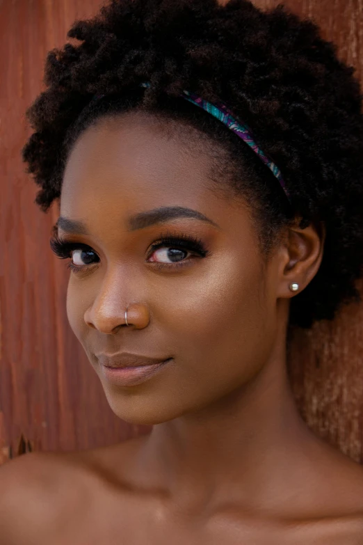 a woman standing in front of a wooden wall, trending on pexels, afrofuturism, chiseled jawline, nose ring, high angle closeup portrait, natural hair