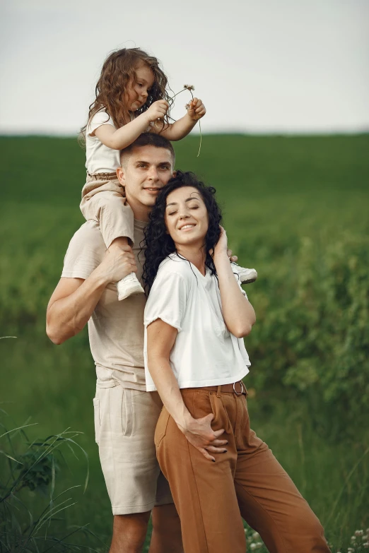 a man holding a little girl on his shoulders, pexels contest winner, portrait of family of three, in a open green field, brown curly hair, maxim sukharev