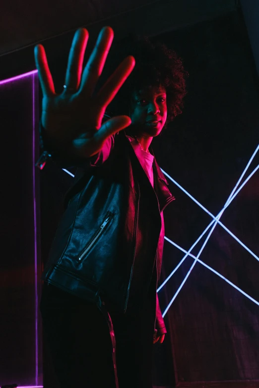 a man standing in front of a neon light, an album cover, by Cosmo Alexander, pexels, leather clothes, afro futuristic, reflecting light in a nightclub, with a cool pose