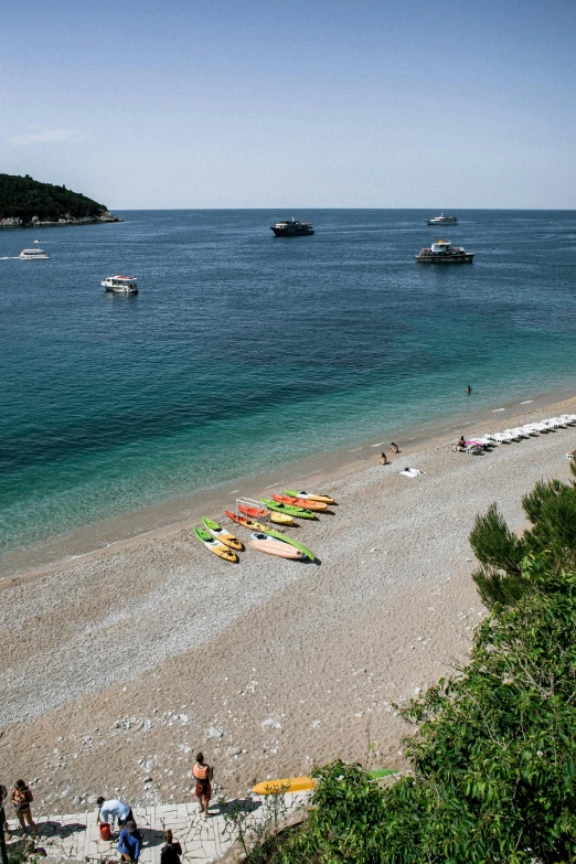 a group of people standing on top of a sandy beach, croatian coastline, small canoes, lush surroundings, square