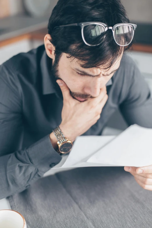 a man sitting at a table reading a piece of paper, pexels contest winner, wearing business casual dress, sleepy, man with beard, thumbnail