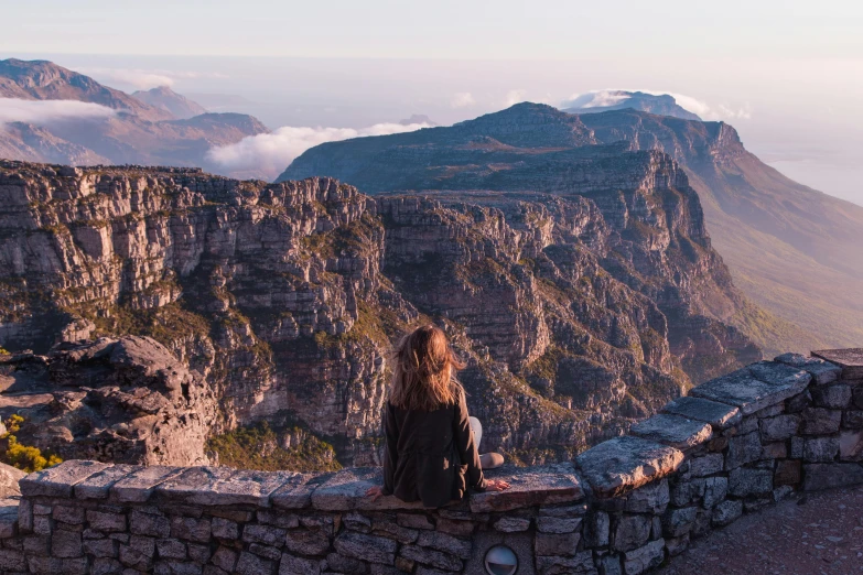 a woman sitting on top of a stone wall, pexels contest winner, south african coast, mountain ranges, photo of emma watson, “the ultimate gigachad