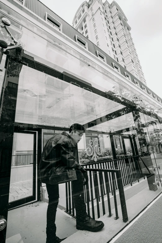 a black and white photo of a man standing in front of a building, unsplash, realism, bus stop, lots of glass details, exiting store, promo image