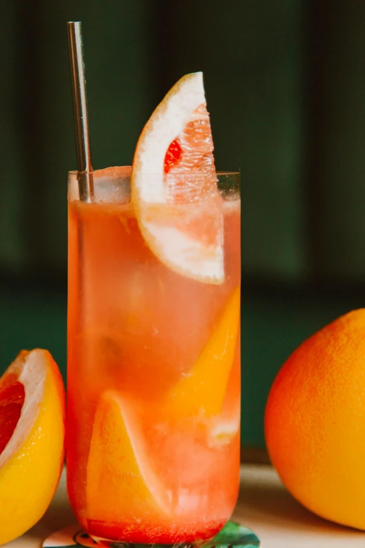a drink sitting on top of a table next to grapefruits, zoomed in, pink and orange, half moon, tall