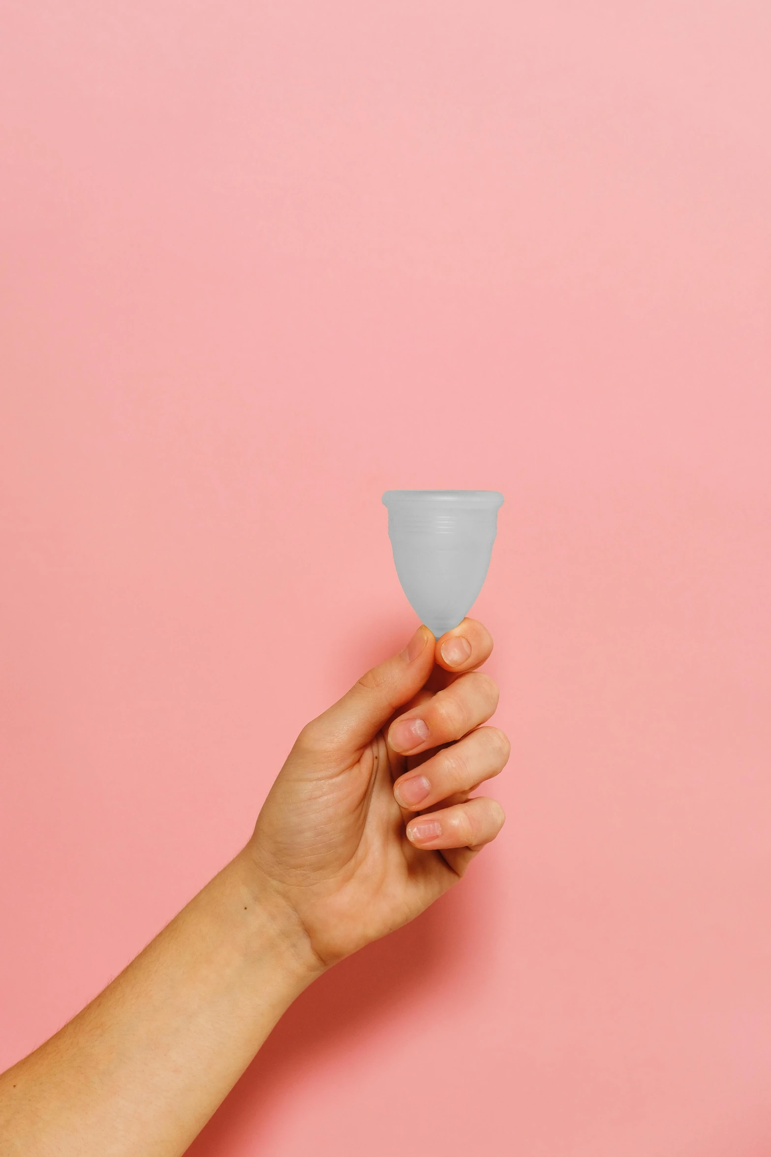 a hand holding a cup against a pink background, plasticien, grey, cone shaped, silicone skin, hero shot