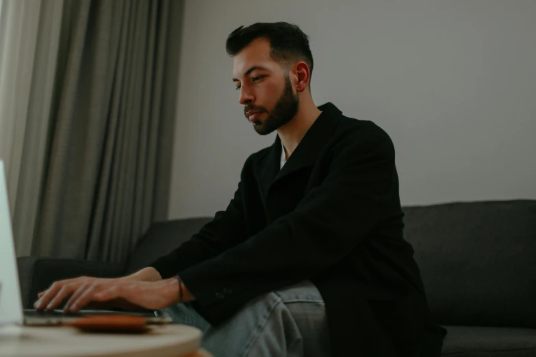 a man sitting on a couch using a laptop computer, by Emma Andijewska, pexels contest winner, looking serious, avatar image, man in black, low quality photo