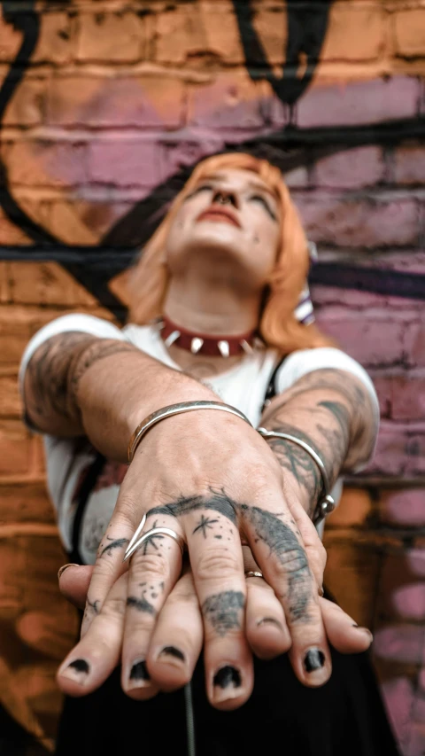 a woman standing in front of a graffiti covered wall, an album cover, by Drew Tucker, trending on pexels, graffiti, photo of a hand jewellery model, gangrel, single pair of hands, leeloo