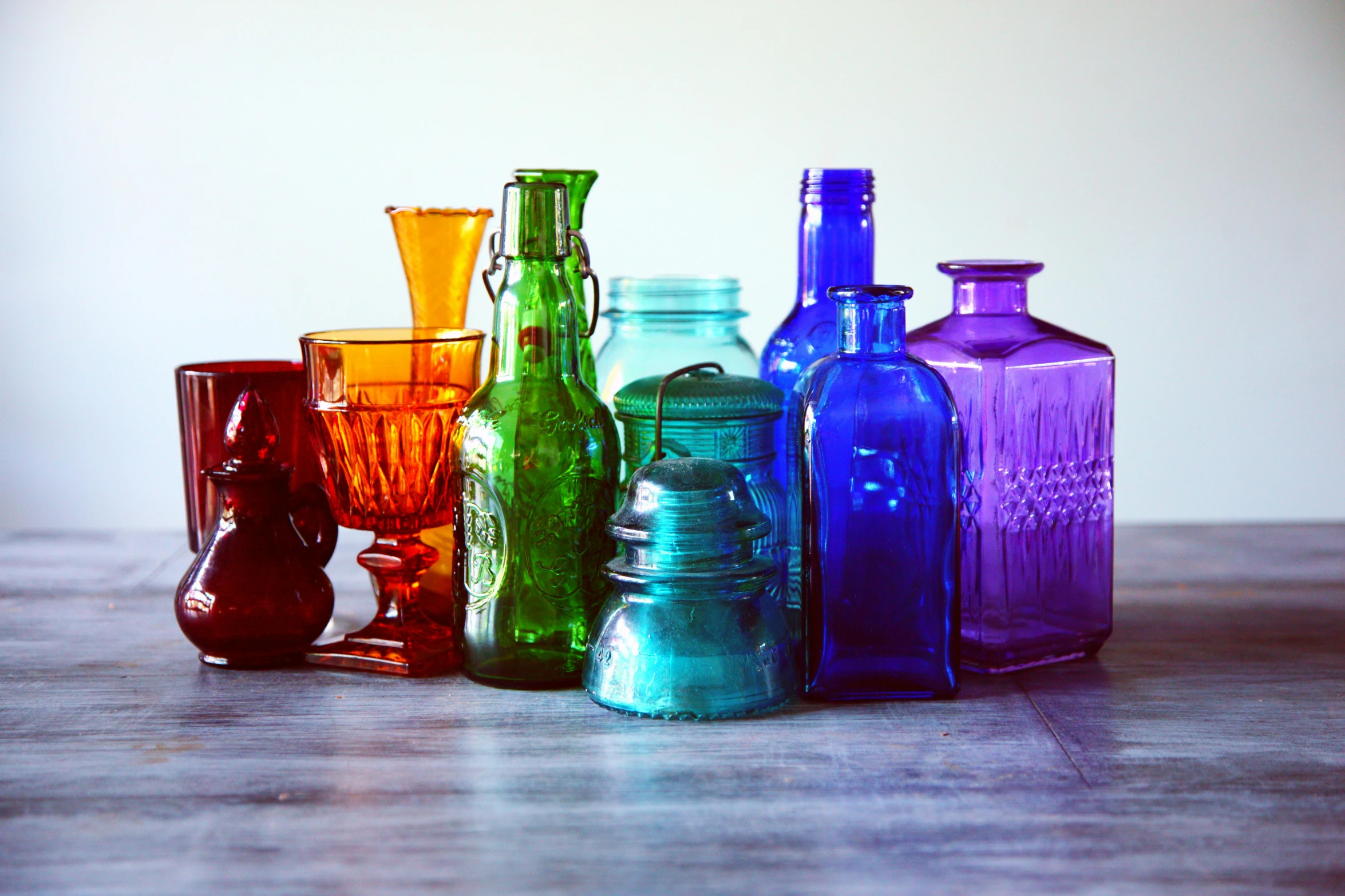 a group of colorful glass bottles sitting on top of a wooden table, inspired by Doug Ohlson, trending on pexels, renaissance, side light, indigo rainbow, colorful signs, set against a white background