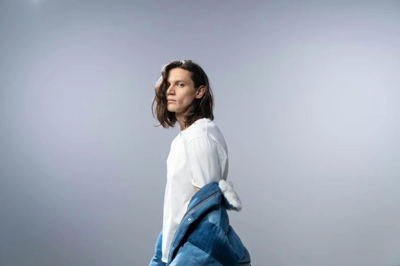 a woman in a white shirt and blue jeans, an album cover, by Nina Hamnett, photorealism, androgynous male, orelsan, relaxed. blue background, casual pose