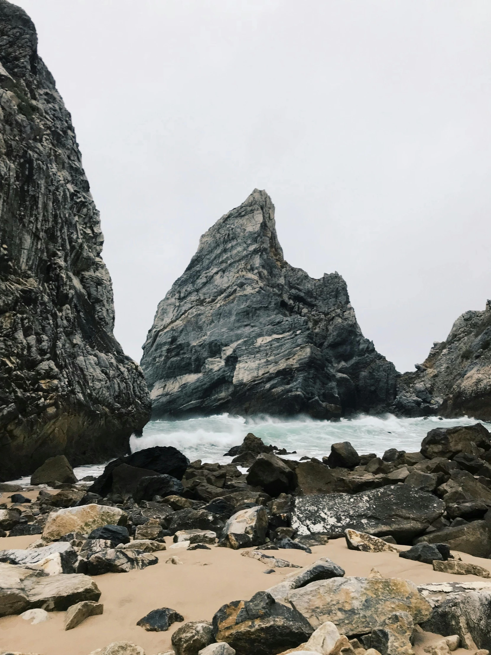 a couple of rocks sitting on top of a sandy beach, steep cliffs, devils horns, profile image, trending photo