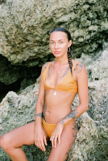 a woman in a bikini sitting on a rock, by Nina Hamnett, trending on pexels, renaissance, wearing yellow croptop, bone jewellery, wearing leather swim suite, tanned skintone