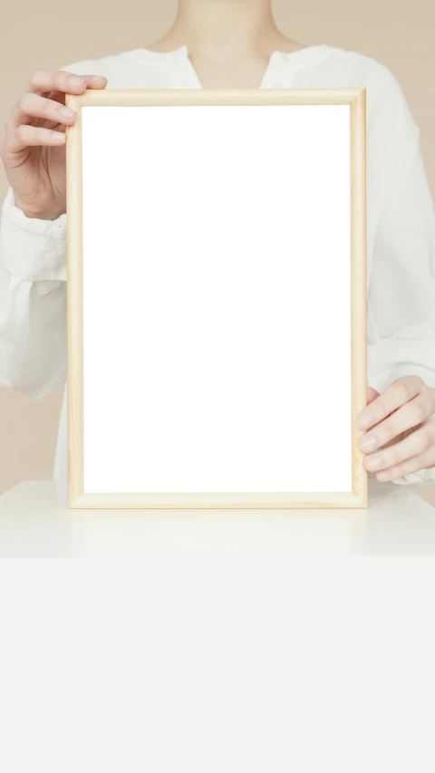 a woman holding a picture frame in front of her face, a poster, inspired by Agnes Martin, trending on pexels, postminimalism, white table, high quality photo, thumbnail, background image