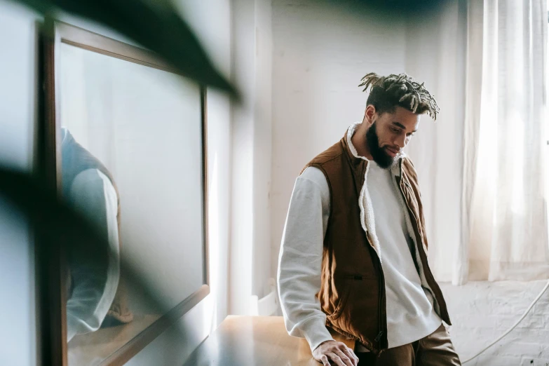 a man in a white shirt and brown vest, an album cover, inspired by Frank Mason, trending on pexels, standing near a window, wearing a track suit, dreads, sitting on a mocha-colored table