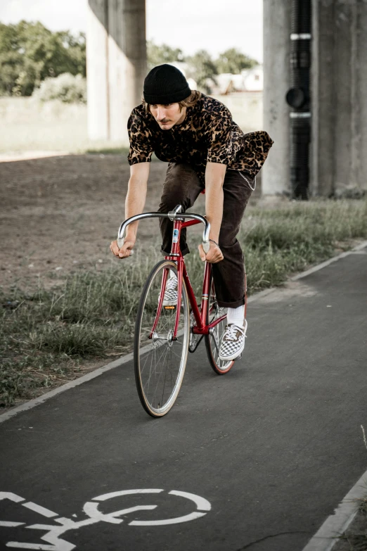 a man riding a bike down a street, inspired by Seb McKinnon, dribble, red shirt brown pants, federation clothing, paisley, aerodynamic