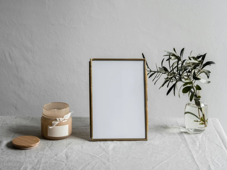 a picture frame sitting on top of a table next to a vase, a picture, unsplash, brass sheet, in front of white back drop, jar on a shelf, handcrafted paper background