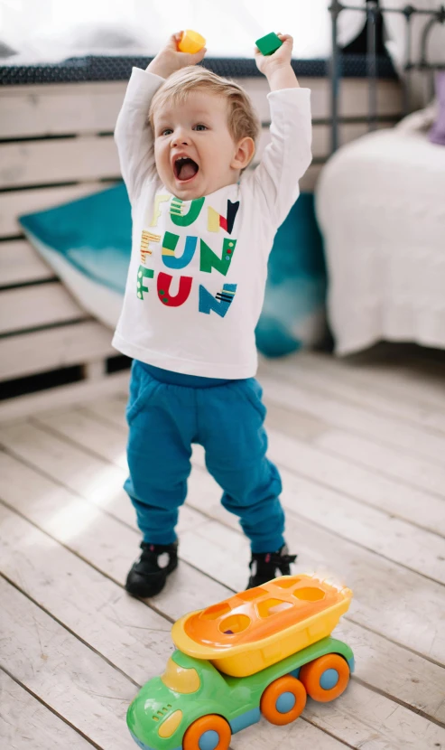 a little boy standing on top of a wooden floor, inspired by Tomi Ungerer, pexels contest winner, graffiti, laughing out loud, funny jumbled letters, printed on a cream linen t-shirt, cheerful colours