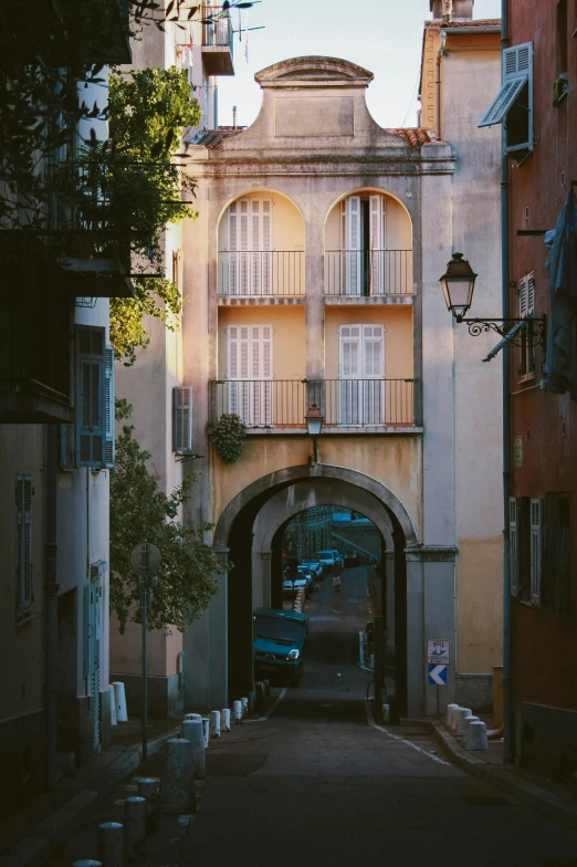 a narrow street with a building in the background, inspired by Luis Paret y Alcazar, pexels contest winner, renaissance, arched doorway, summer evening, parking in the street, sunfaded