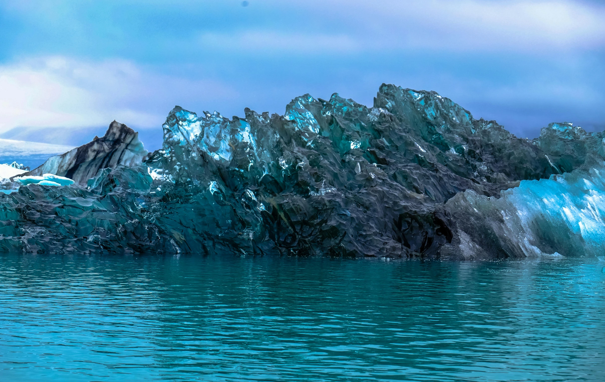 a large iceberg in the middle of a body of water, an album cover, unsplash, tones of blue and green, metallic reflections, rock formations, reykjavik