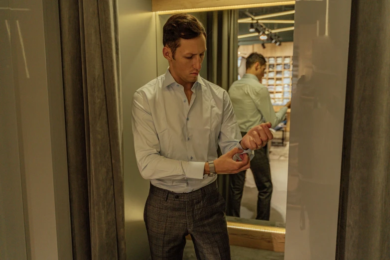 a man standing in front of a mirror looking at his cell phone, dress shirt, james collinson, official store photo, nikolay