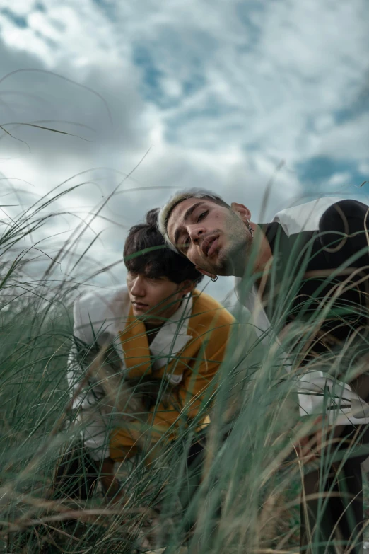 a group of young men sitting on top of a grass covered field, an album cover, unsplash, renaissance, portrait of two people, windy mood, highlight, lesbians