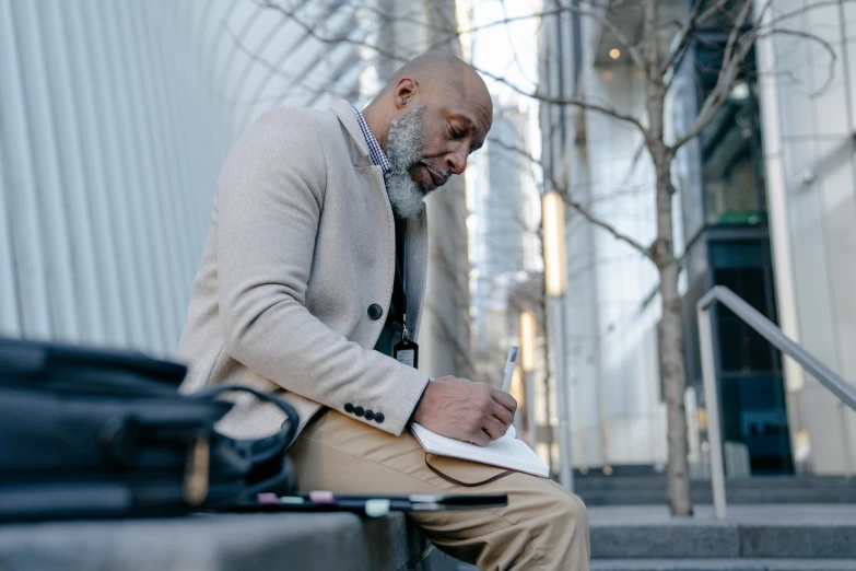 a man sitting on a bench writing on a piece of paper, inspired by William H. Mosby, pexels contest winner, in city street, thumbnail, 1 / 4 portrait, high quality image