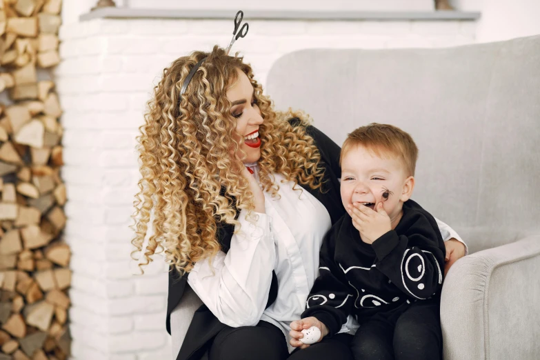 a woman and a child sitting on a couch, a cartoon, pexels, antipodeans, long curly blond hair, with black, 2 years old, fashionable