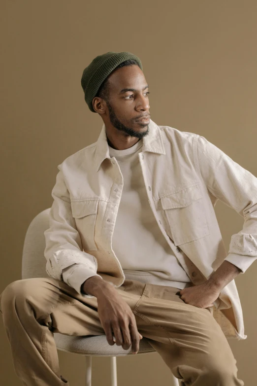 a man sitting on top of a white chair, an album cover, inspired by Barthélemy Menn, trending on pexels, photorealism, wear's beige shirt, baggy clothing and hat, looking to the side off camera, wearing a linen shirt