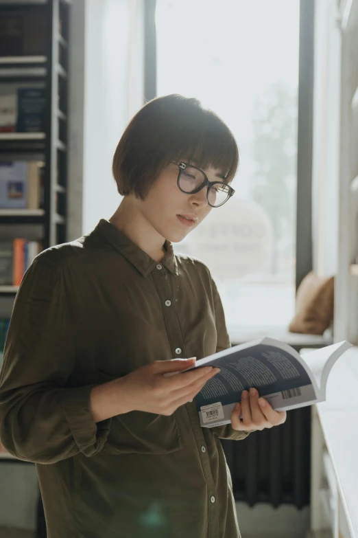 a woman standing in front of a window reading a book, by Jang Seung-eop, pexels contest winner, nerdy appearance, avatar image, asian male, russian academic