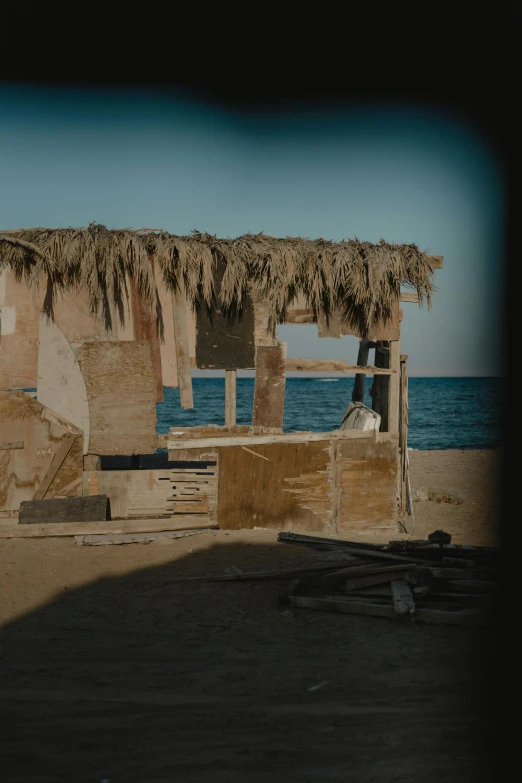 a hut sitting on top of a sandy beach next to the ocean, unsplash, renaissance, damaged structures, from egypt, profile image, vhs footage of a movie set