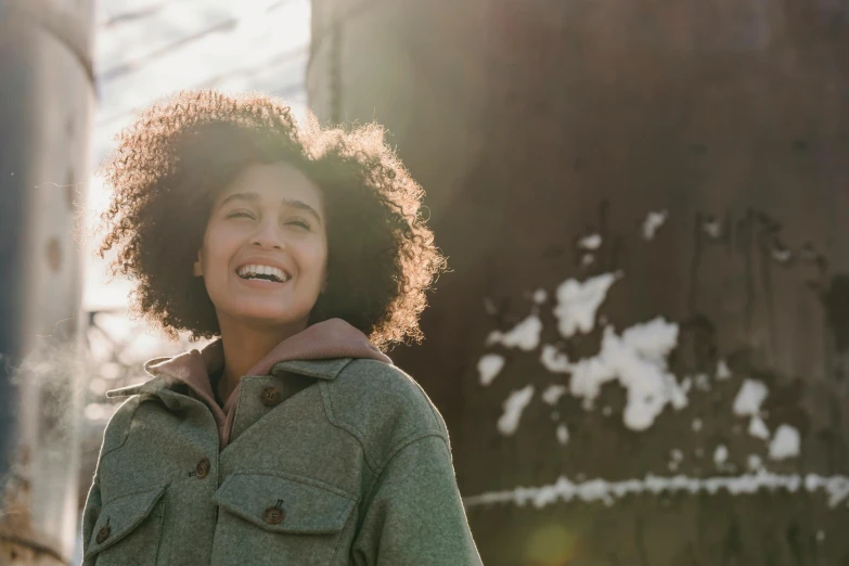 a woman in a green jacket smiles at the camera, trending on pexels, winter sun, with afro, happy girl, brown