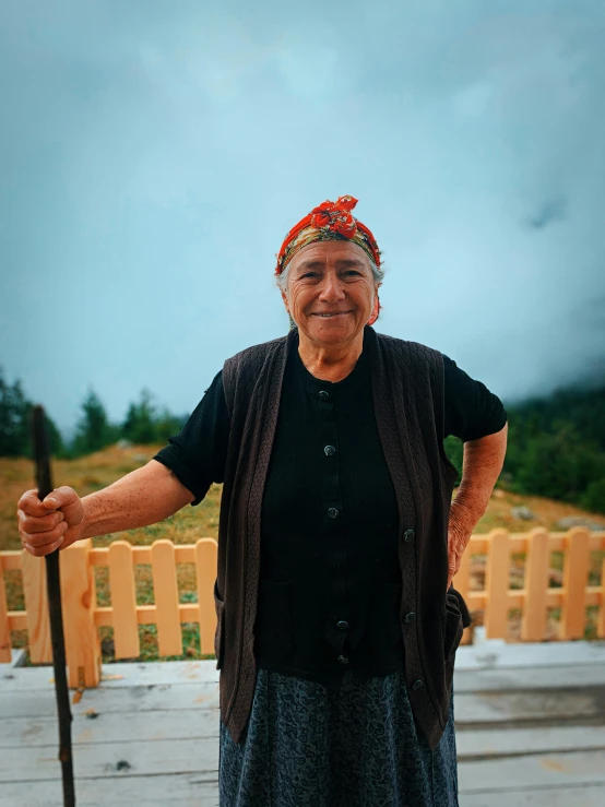 a woman standing on a deck with a cane, a picture, by Kristian Zahrtmann, pexels contest winner, turkey, smiling at camera, farmer, covered in clouds