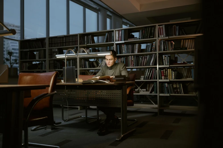 a man sitting at a desk in front of a laptop computer, by Dietmar Damerau, hyperrealism, in a gloomy library, reza afshar, julian ope, high quality photo