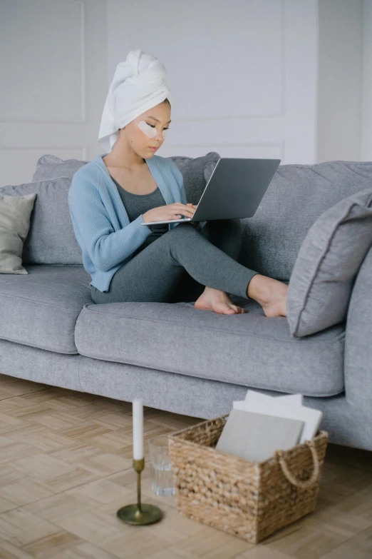 a woman sitting on a couch using a laptop, inspired by Li Di, pexels contest winner, aestheticism, turban, wearing a grey robe, knees upturned, thumbnail