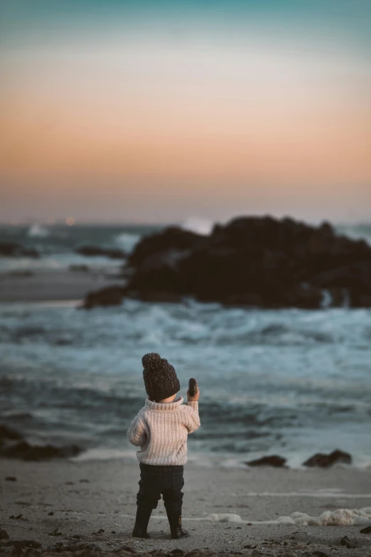 a small child standing on top of a sandy beach, pexels contest winner, magic hour, looking out at the ocean, slightly pixelated, smol