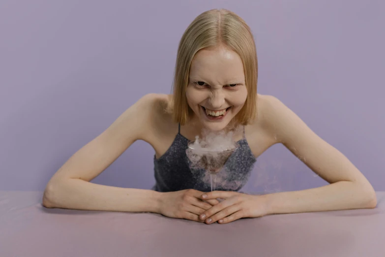 a woman sitting at a table with smoke coming out of her mouth, by Attila Meszlenyi, pexels contest winner, surrealism, greta thunberg smiling, purple liquid, on a pale background, fluffy body