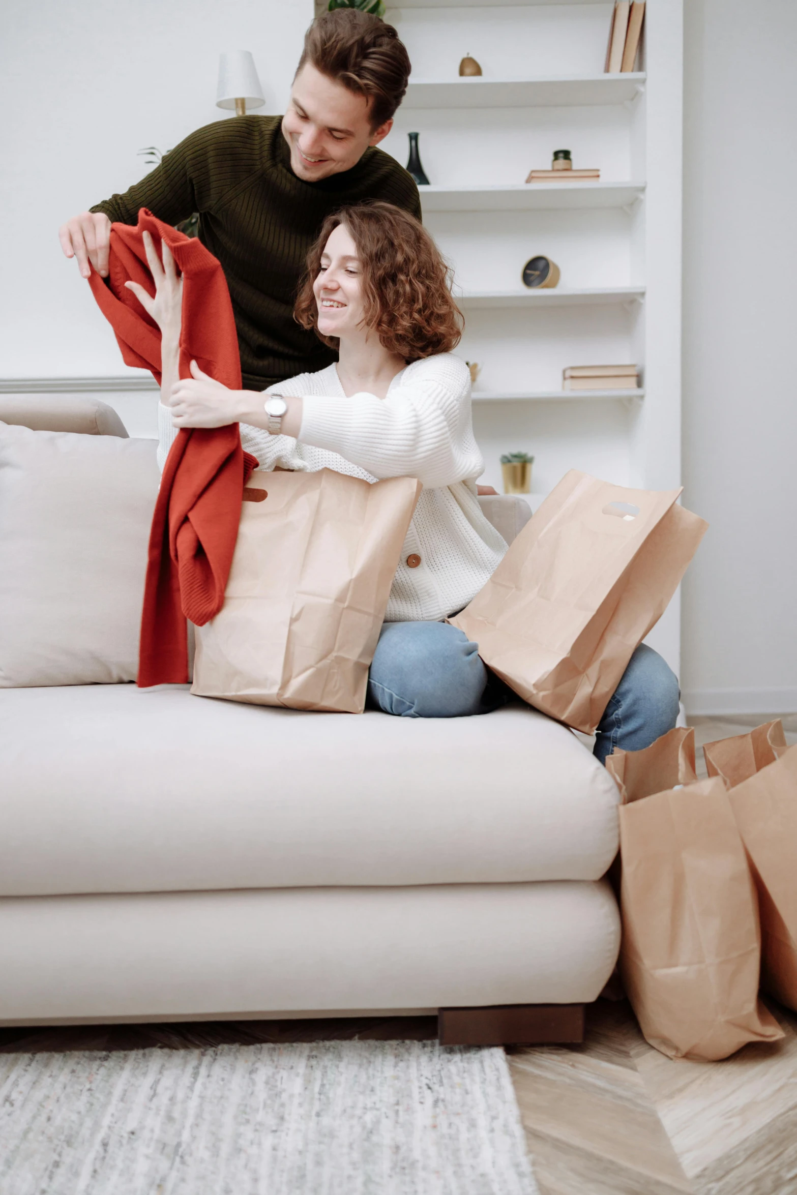 a man and woman sitting on a couch with shopping bags, by Everett Warner, pexels contest winner, happening, touching her clothes, throw pillows, woman holding another woman, plain background