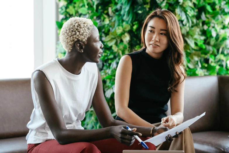 two women sitting on a couch talking to each other, by Lee Loughridge, trending on pexels, hurufiyya, sitting in office, adut akech, sydney park, sitting on a mocha-colored table