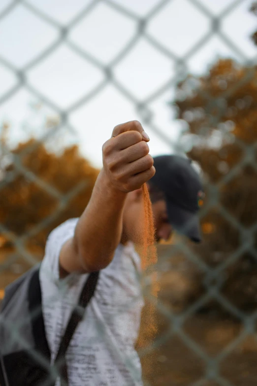 a man holding his fist up in front of a chain link fence, by Niko Henrichon, pexels contest winner, taking tobacco snuff, college, slightly pixelated, nature outside