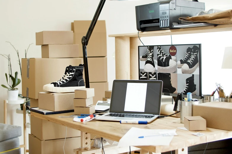 a laptop computer sitting on top of a wooden desk, inspired by Sarah Lucas, inside a cluttered art studio, sneaker design, cardboard, office furniture