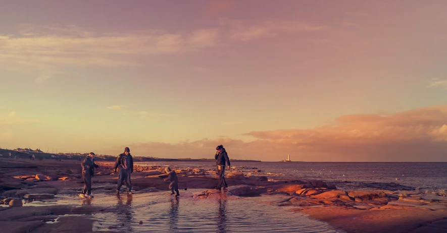 a group of people standing on top of a sandy beach, in the sunset, rock pools, family friendly, retro vibe