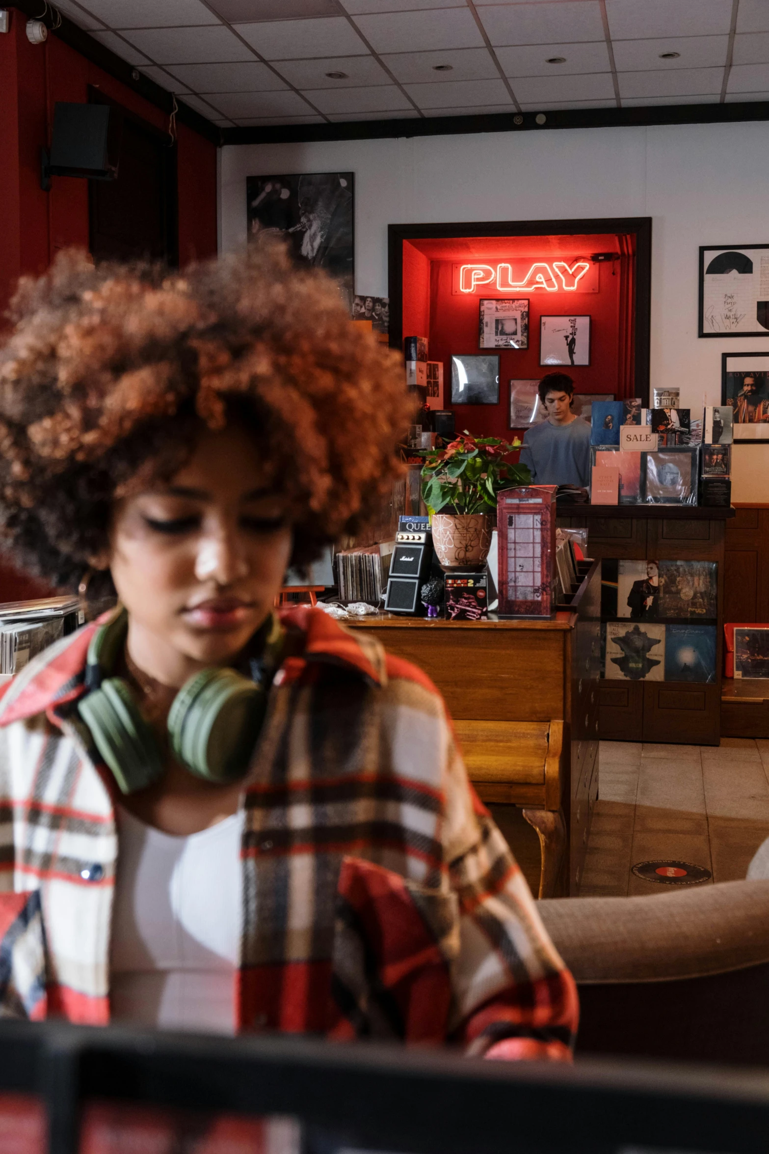 a woman sitting in front of a laptop computer, an album cover, trending on pexels, girl in a record store, red headphones, afro, small hipster coffee shop